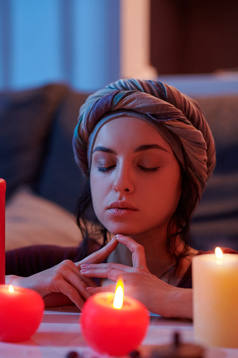 A woman wearing a turban sits peacefully while closing her eyes in front of flickering candles, creating a serene and contemplative atmosphere.